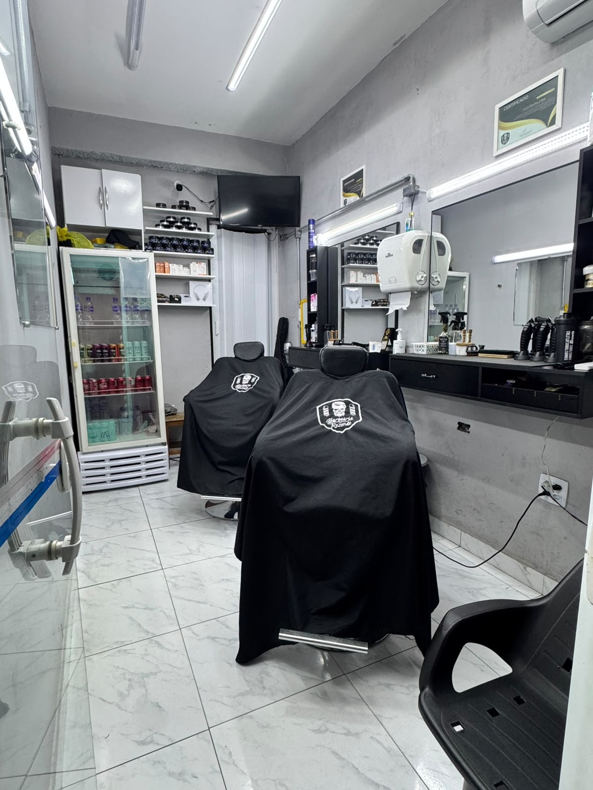 Interior da Barbearia Rezende com cadeiras, espelhos iluminados e capas personalizadas